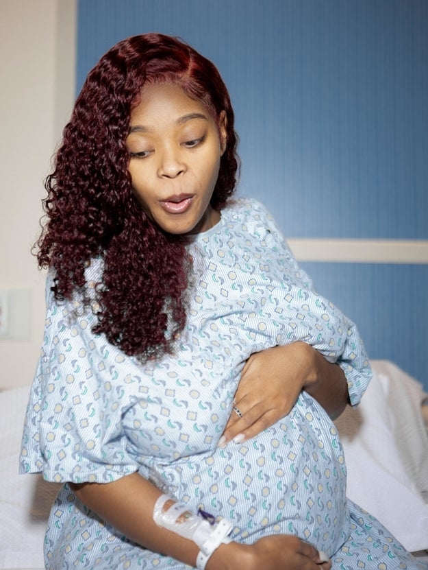 Dee holding her pregnant belly in a hospital gown