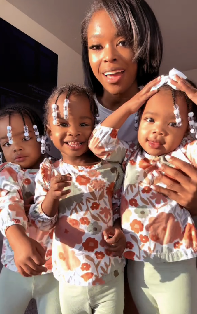 Dee posing with her triplet daughters while they are dressed in the same outfit