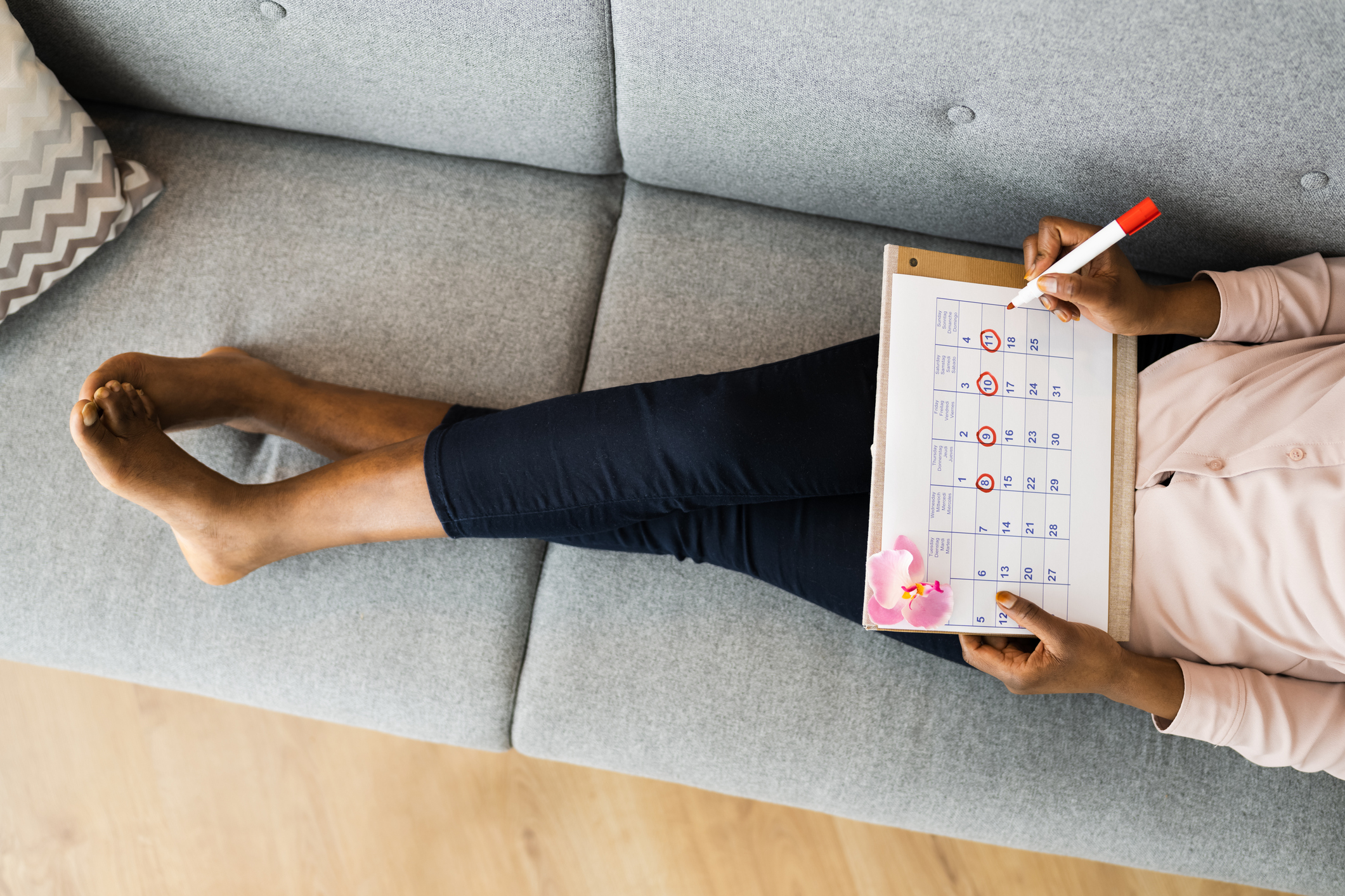 A person tracking their menstrual cycle on a calendar board while sitting on a couch
