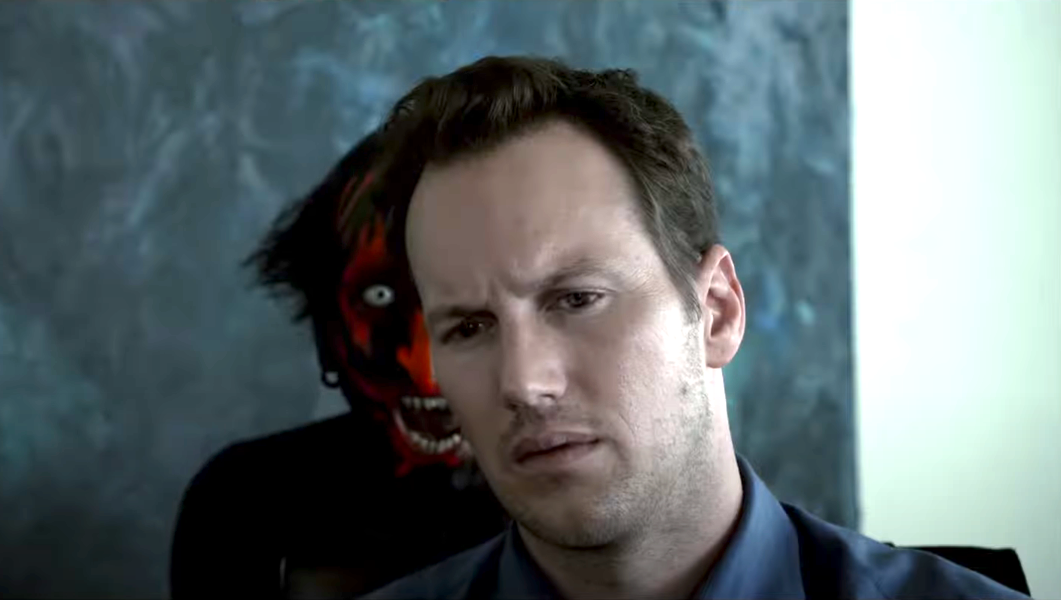 a man sitting at a table while a very scary demon has its mouth wide open behind him