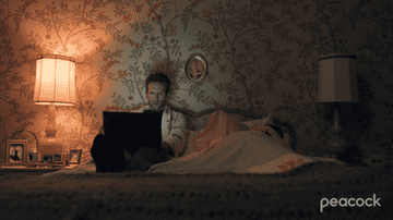 man working on his laptop in bed while a partner sleeps next to him