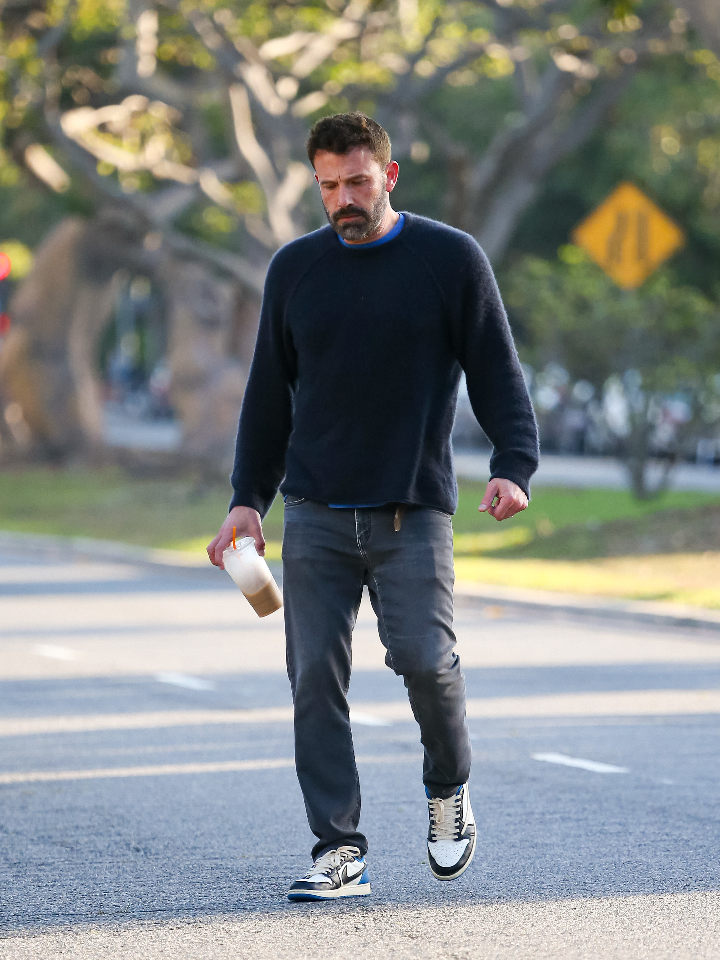 he&#x27;s looking down while he walks and holds an almost empty iced coffee