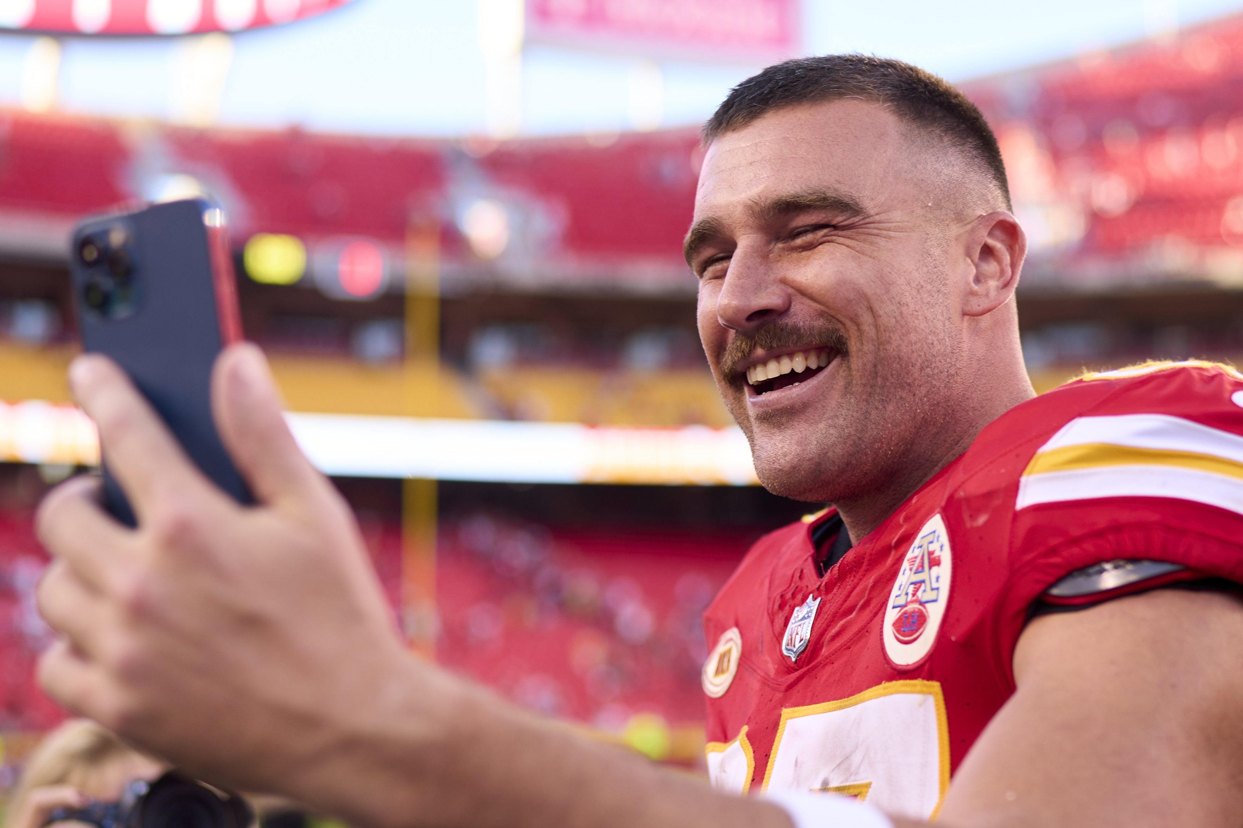 Close-up of Travis smiling in his football jersey and holding up a cellphone