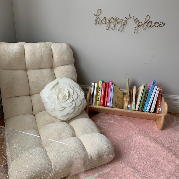 Cozy reading nook with plush chair, decorative cushion, wooden &#x27;happy place&#x27; sign, and a rack of children&#x27;s books