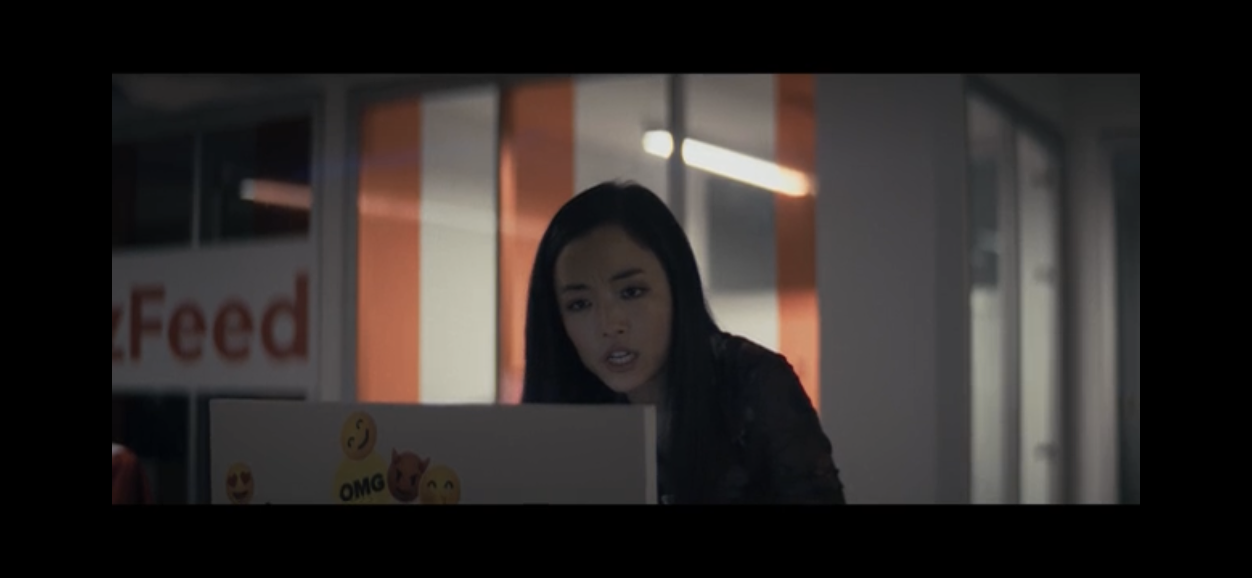 Andrea Bang as Evelyn looking at her computer screen with her mouth open