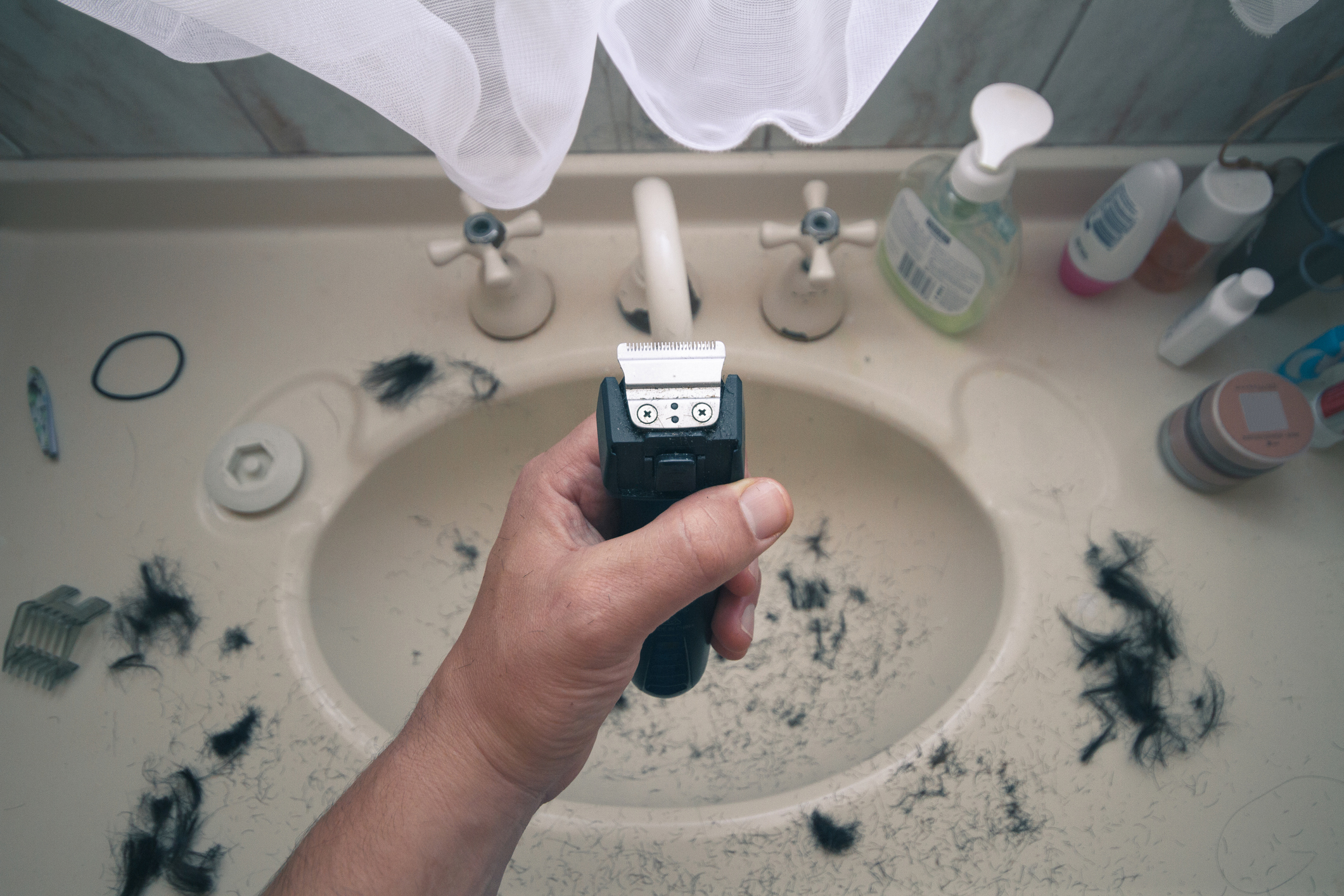 electric razor in someone&#x27;s hand above the sink where hair has fallen