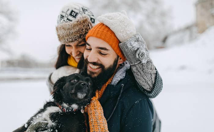 Man and woman smiling in the snow with their dog