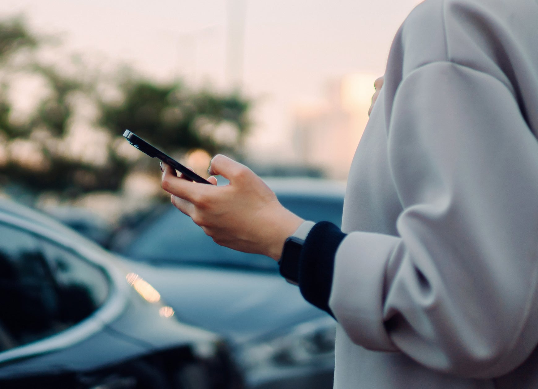 woman holding phone standing by her car