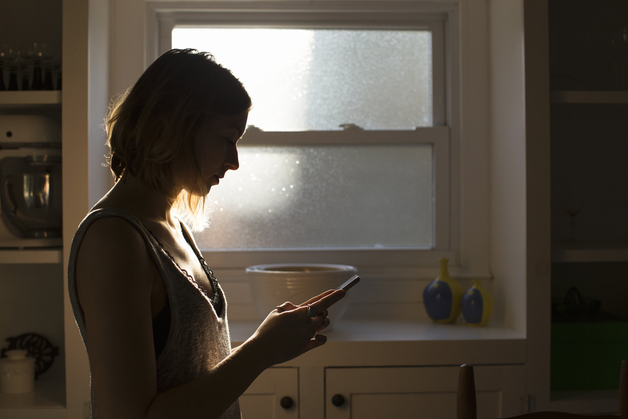 woman texting in a dark kitchen