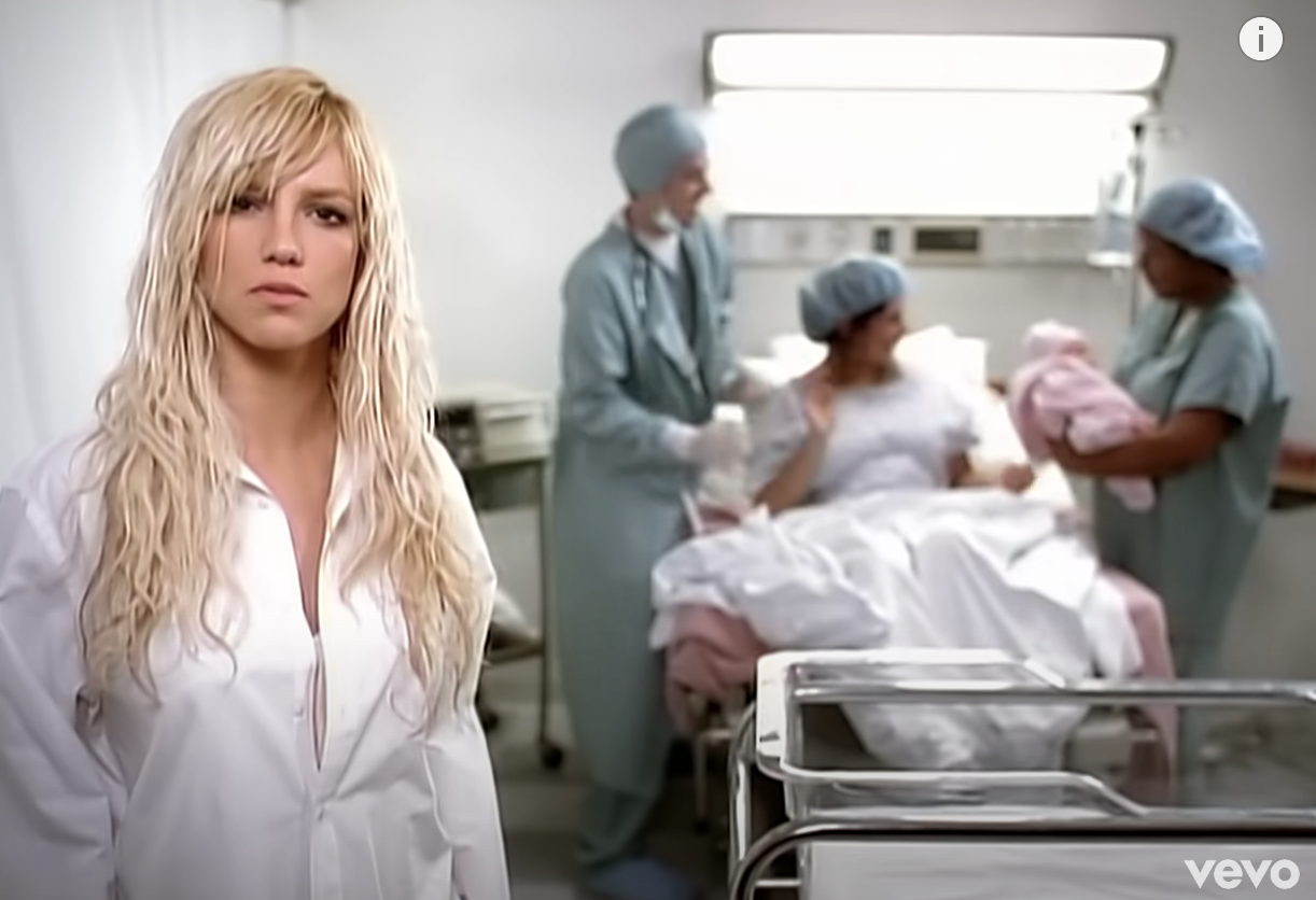 britney with wet hair looking at the camera while a mother gives birth behind her