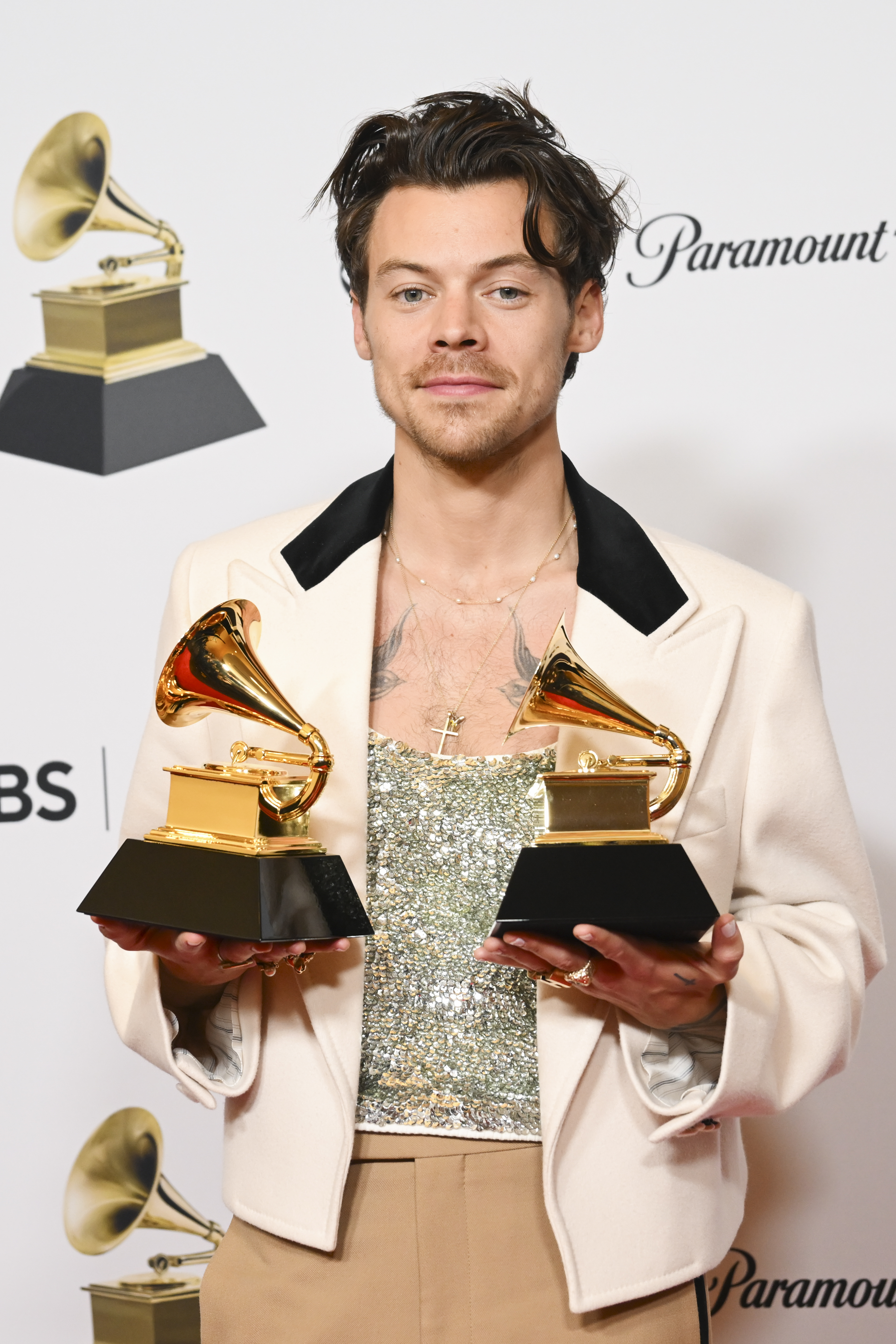 harry with long messy hair holding up two grammys
