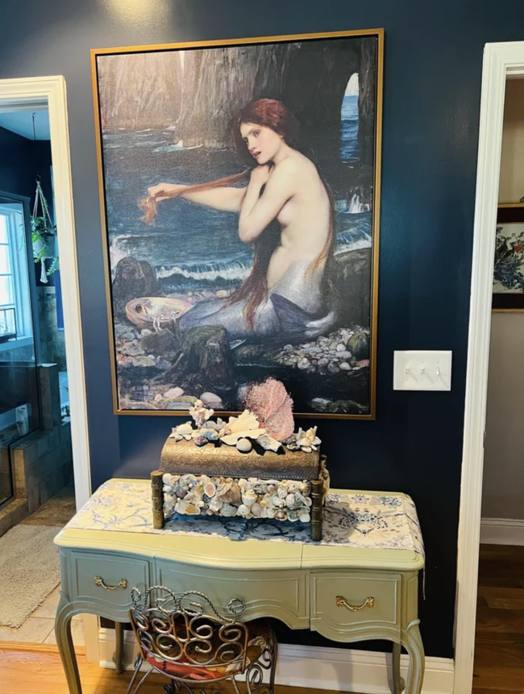 This little space in a home has a portrait of a mermaid in front of a chest decorated with shells