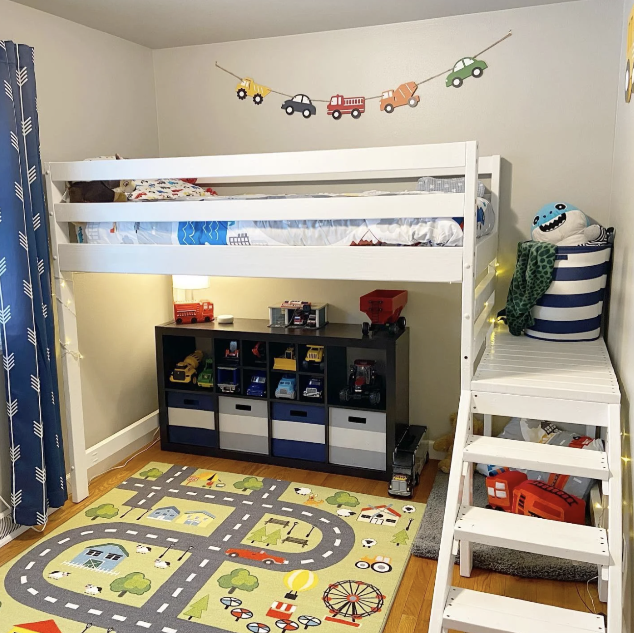 This kid&#x27;s truck-themed bedroom has a road rug, a truck banner, and an array of trucks sitting on a shelf