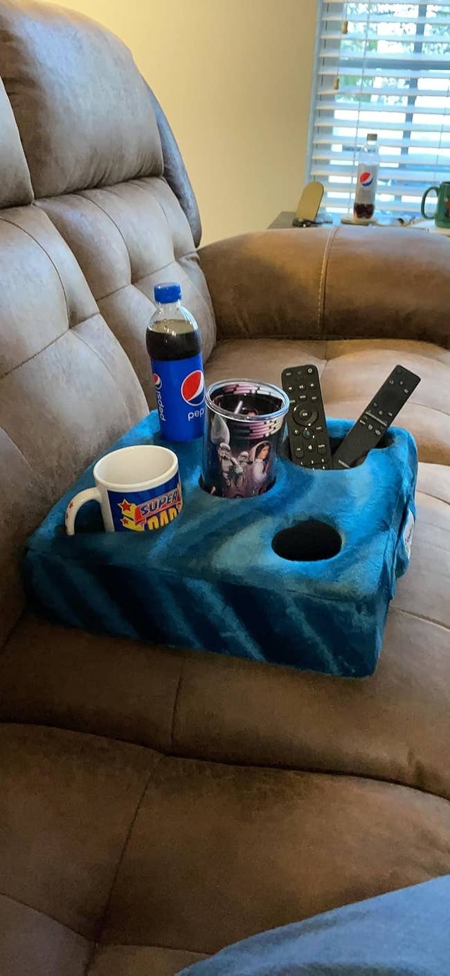 A blue pillow with five holes fitting a can, a drink, a remote control, and a phone