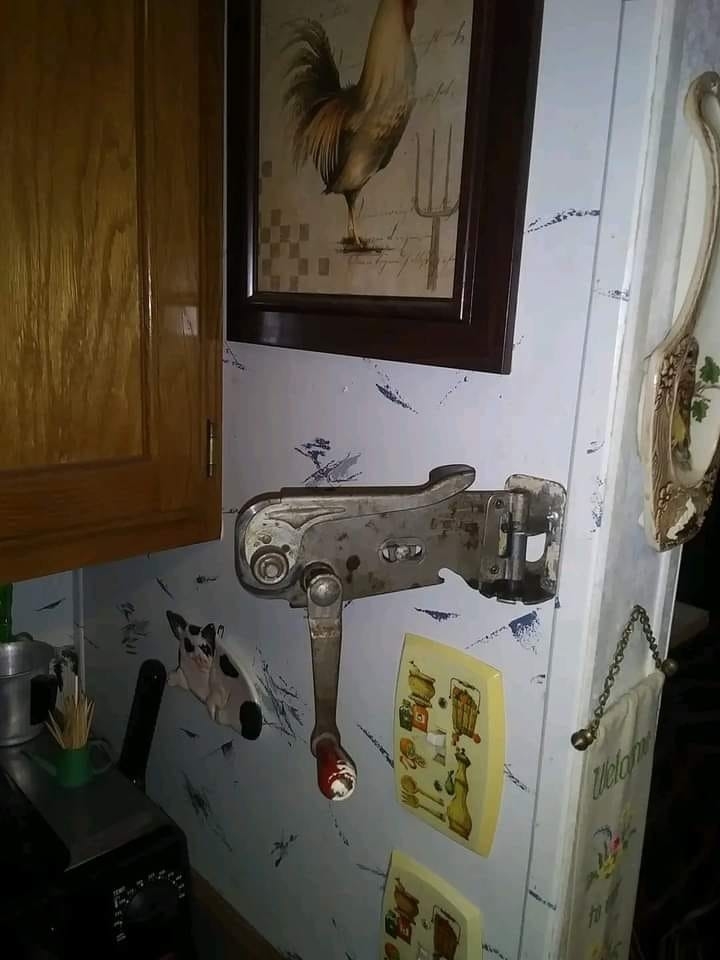A can opener hanging on a wall by a fridge