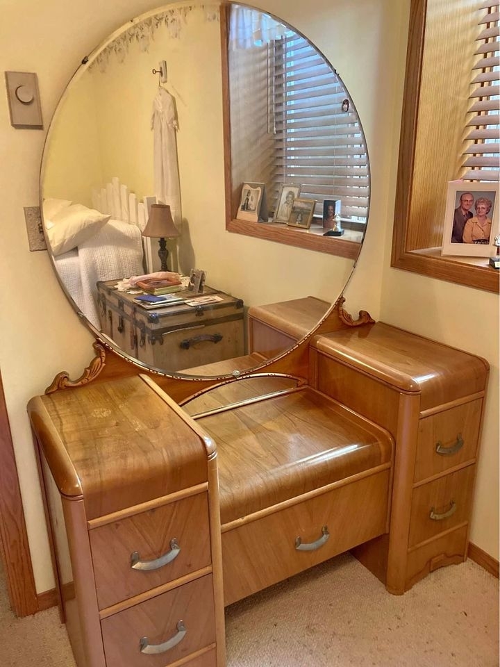 A wood vanity with large oval mirror