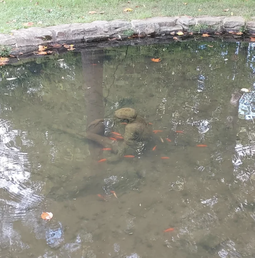 Drab statue of a child sitting in the middle of a pond