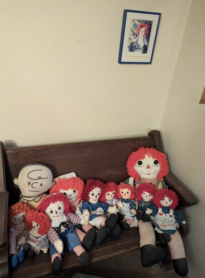 A bench with many Raggedy Ann dolls of different sizes and one Charlie Brown doll