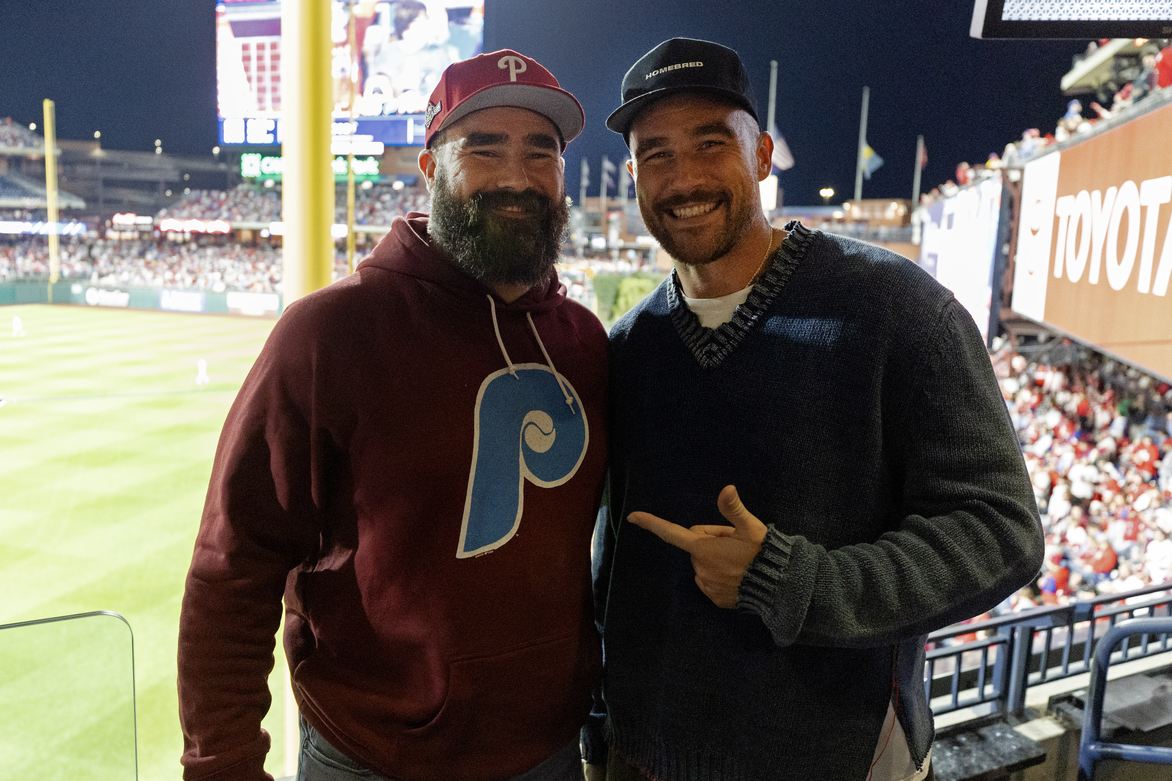 Close-up of Jason and Travis smiling and standing together at a sports stadium