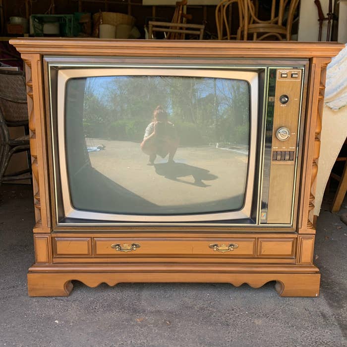 A large TV with a tuner knob and encased in a wood cabinet