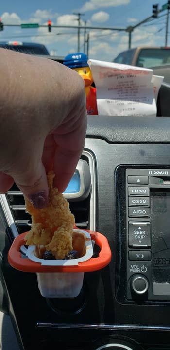 The clip attached to a car vent, with a reviewer dipping a chicken tender into the dauce