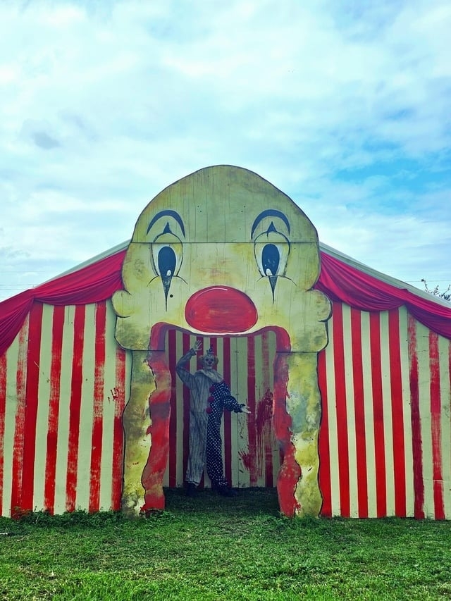A clown waving from the entrance of a carnival attraction