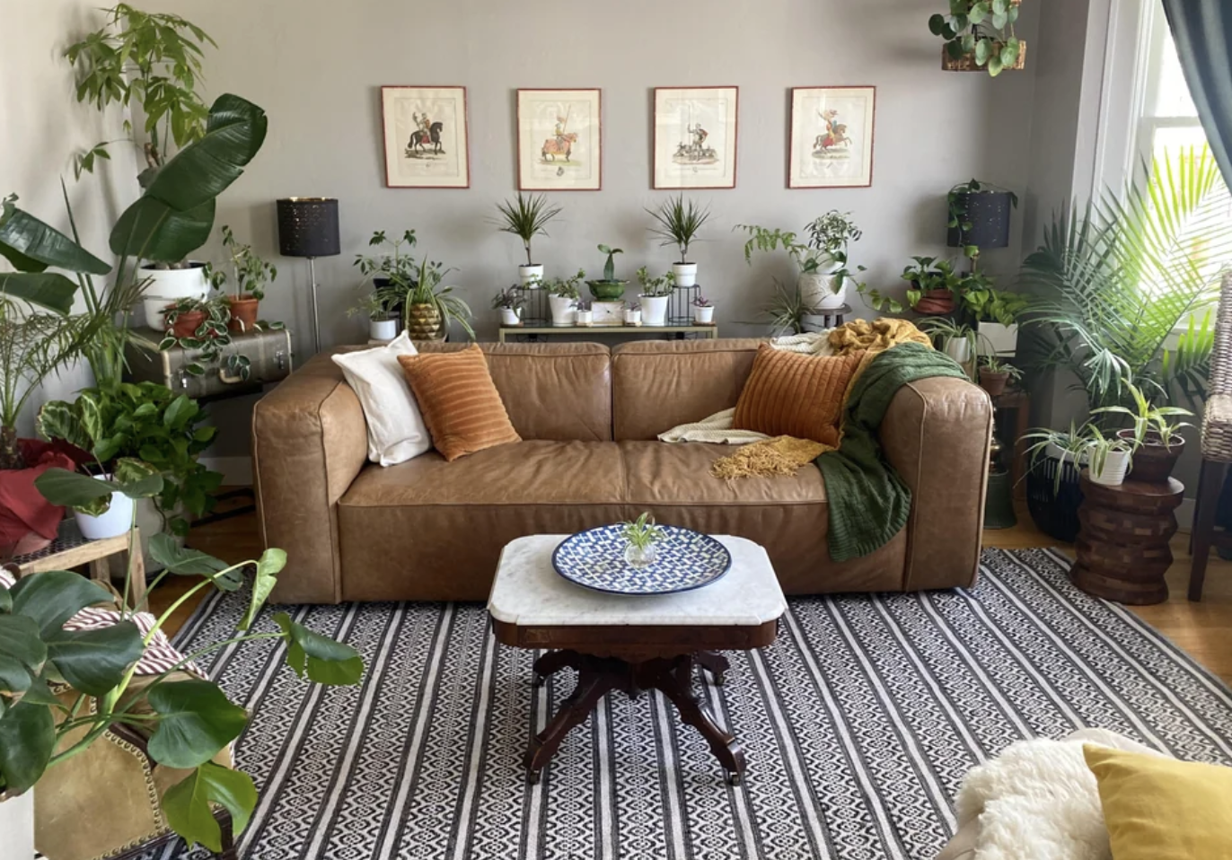 This living room is filled with plants, a statement carpet, and a beautiful brown couch