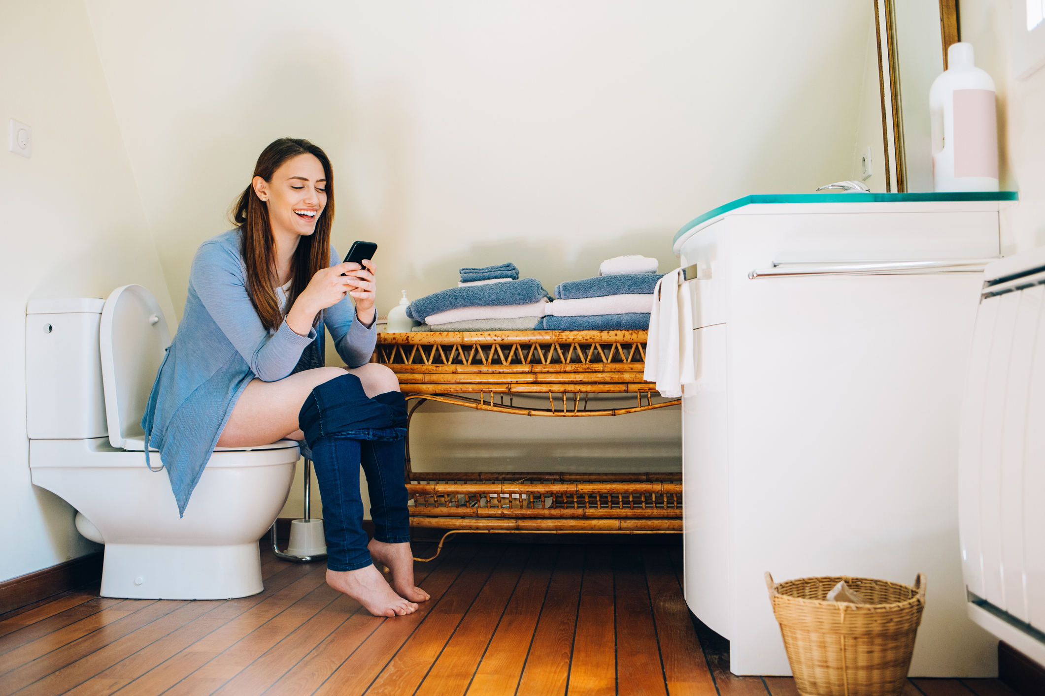 A woman looking at her phone and smiling while sitting on the toilet bowl