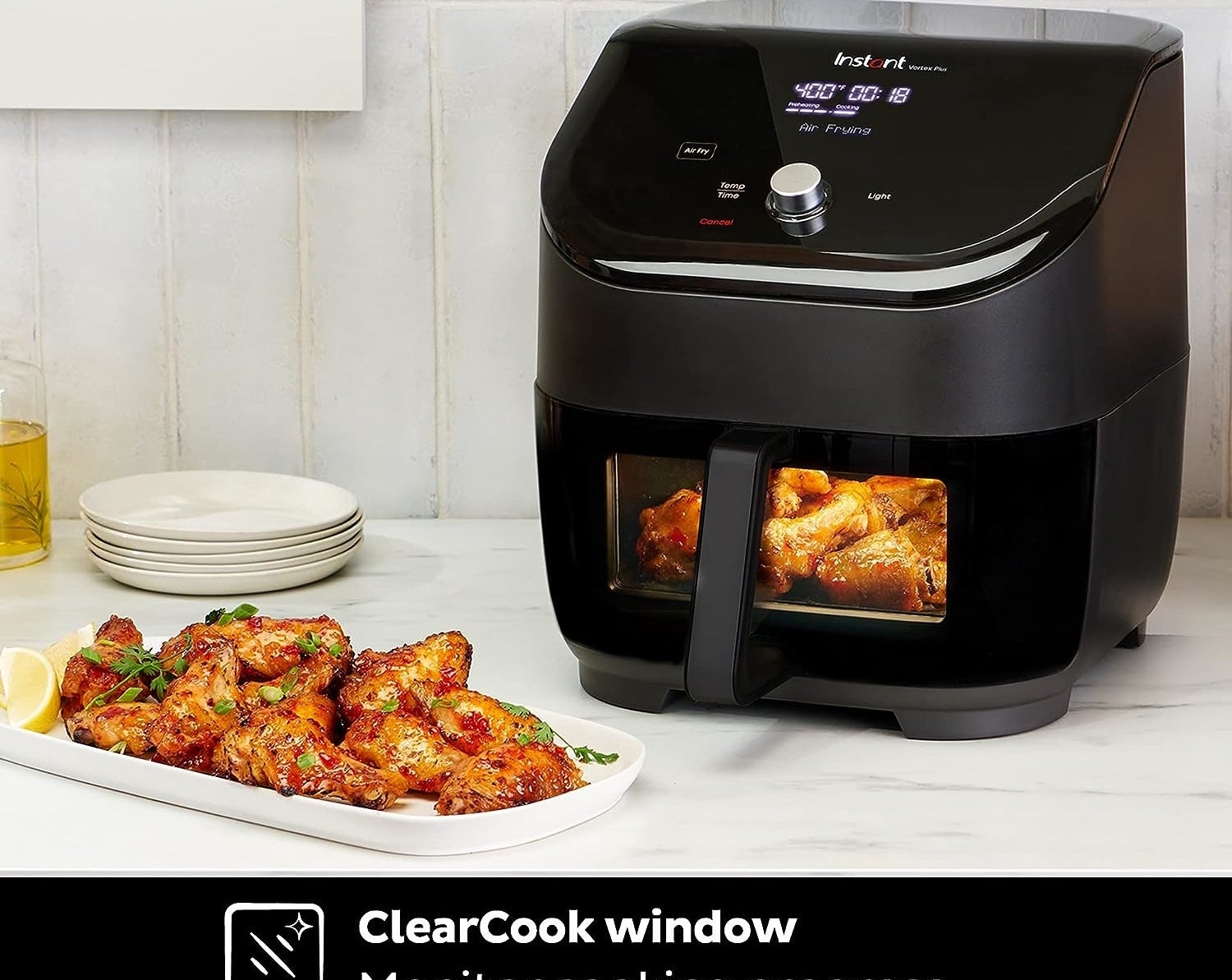 Black air fryer cooking wings next to a plate of freshly cooked wings