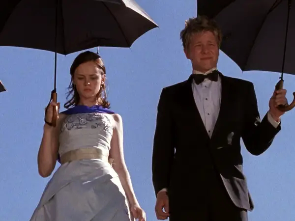 Rory and Logan hold umbrellas while wearing formalwear and look down