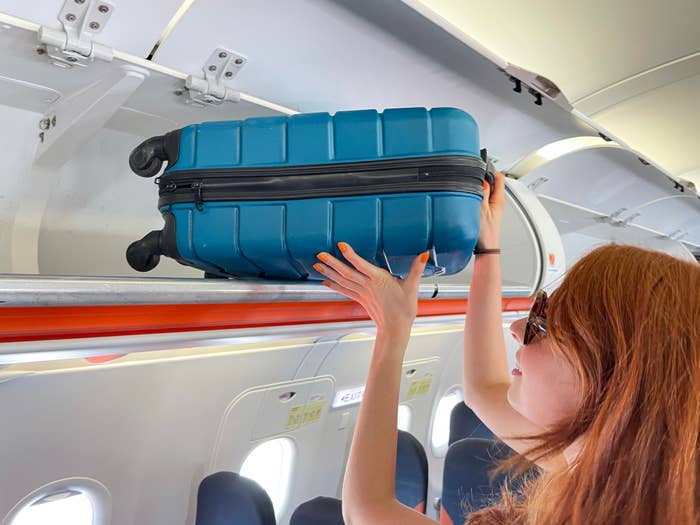 someone putting their carry-on into the overhead compartment of a plane