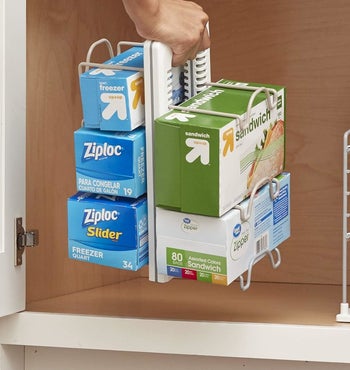 model putting the organizer in a cabinet, which is holding various boxes of plastic bags