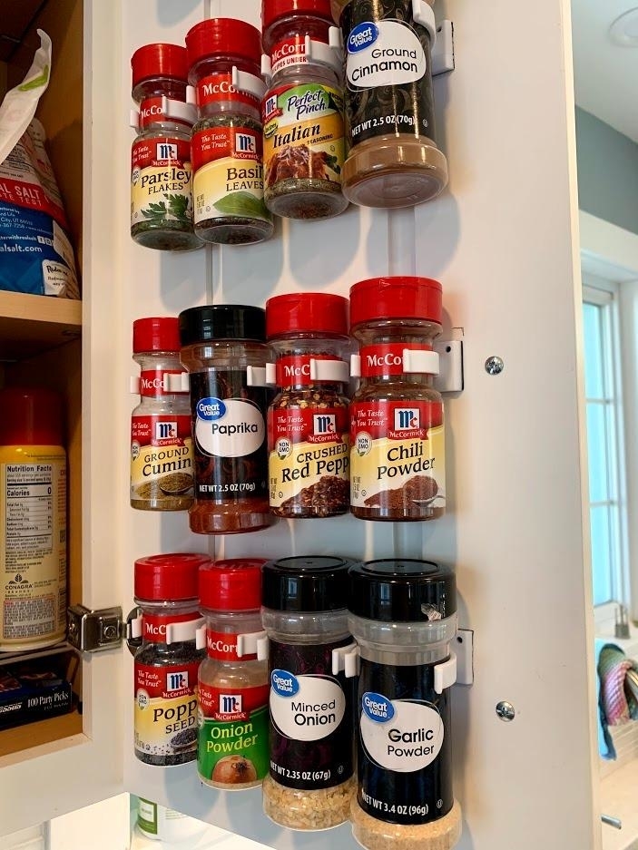 reviewer&#x27;s sets of gripper clips hanging inside a cabinet door holding spices