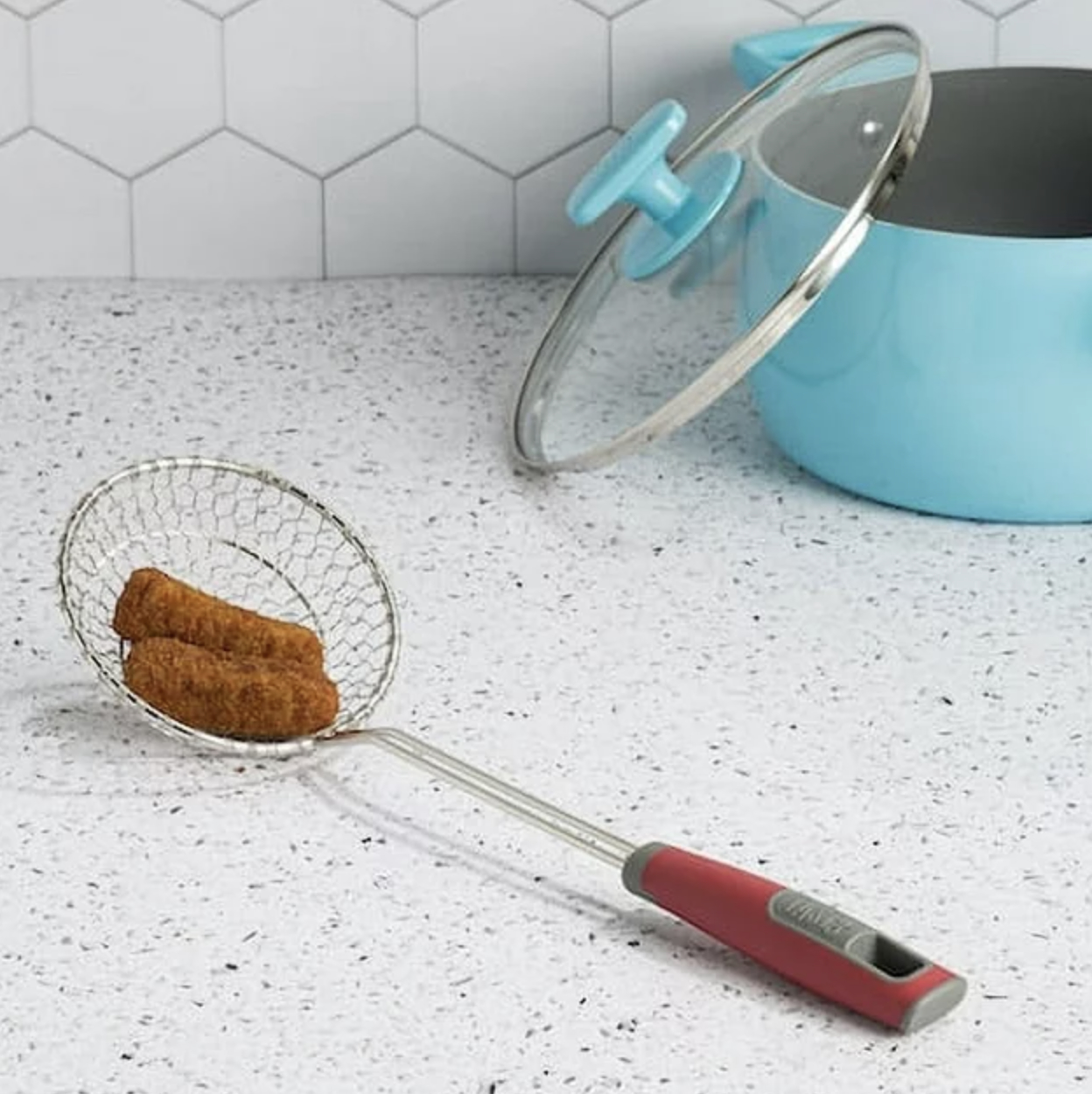 The steel skimmer spoon resting on countertop with fried mozzarella sticks in basket of spoon