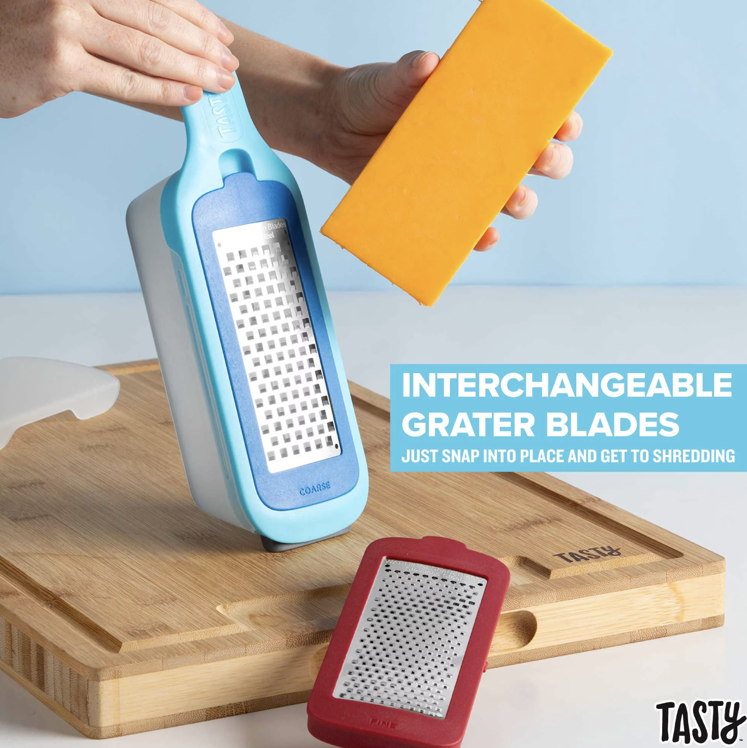 The shredder with course grater blade attached to measuring base as someone begins to shred a block of cheese; red fine blade resting on cutting board