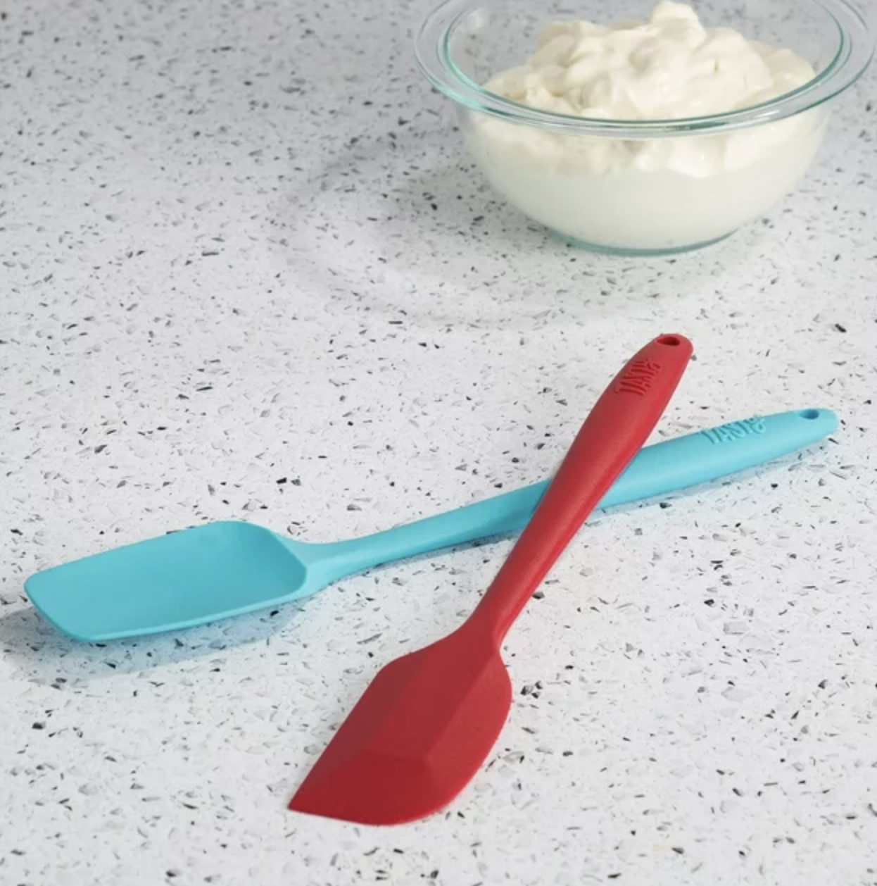 The red and blue spatula on countertop next to bowl of whipped cream