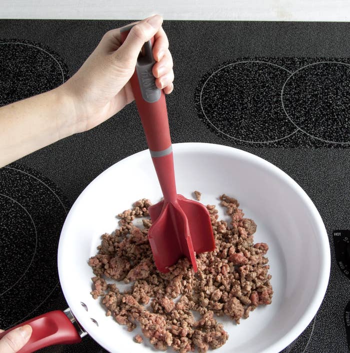 Someone cutting and mixing ground beef in bowl with red meat chopper tool