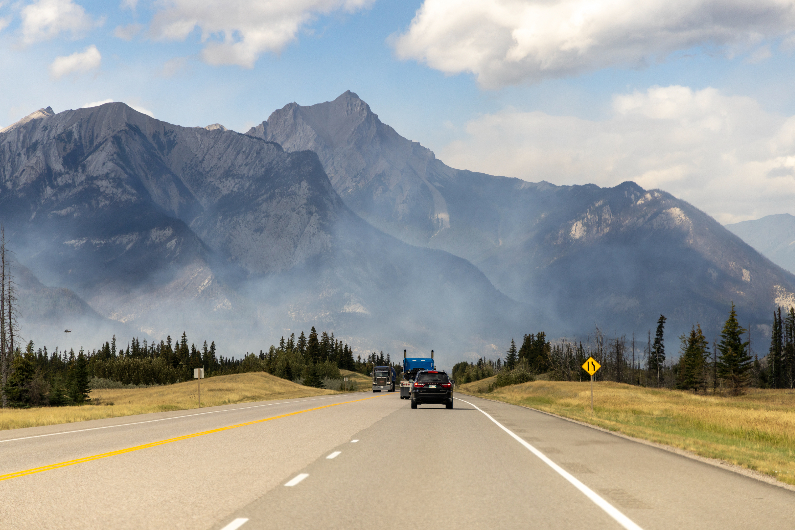 road in Alberta leads to Mountain in distance covered in hazey smoke.