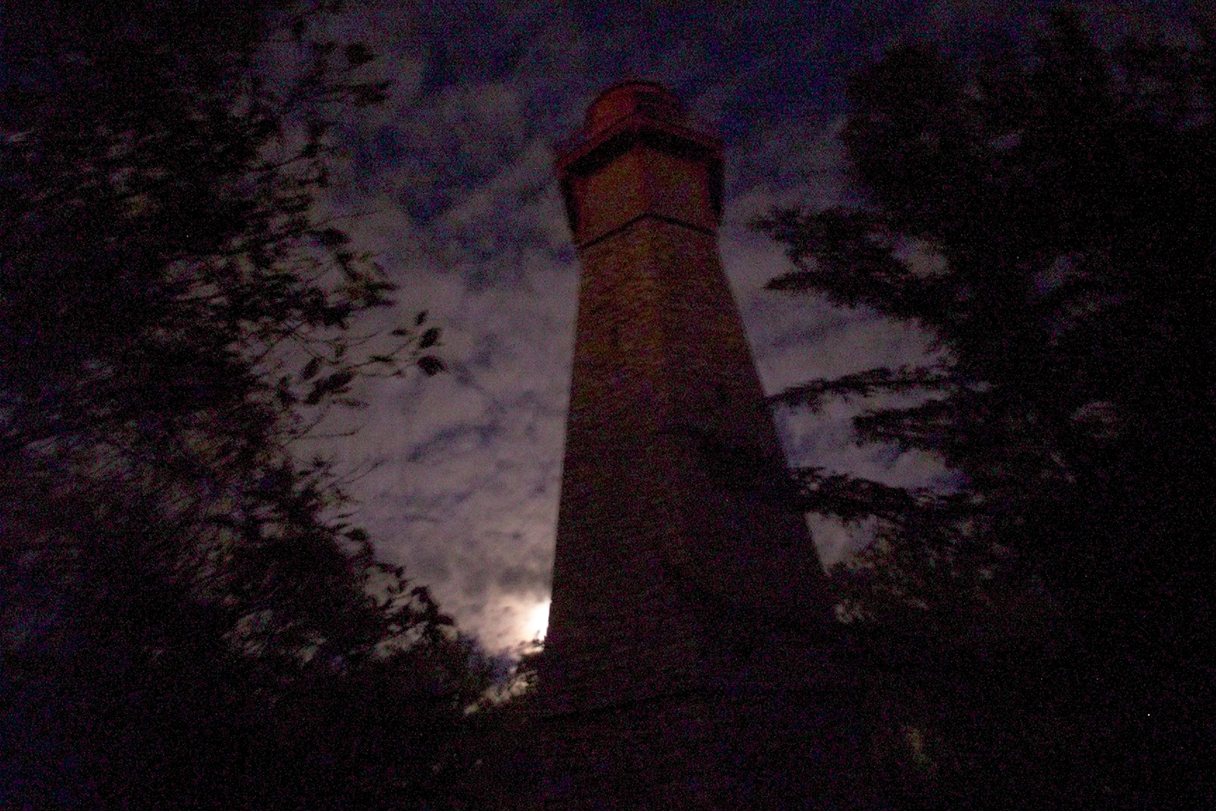 Lighthouse in between forests and against the dark night sky.