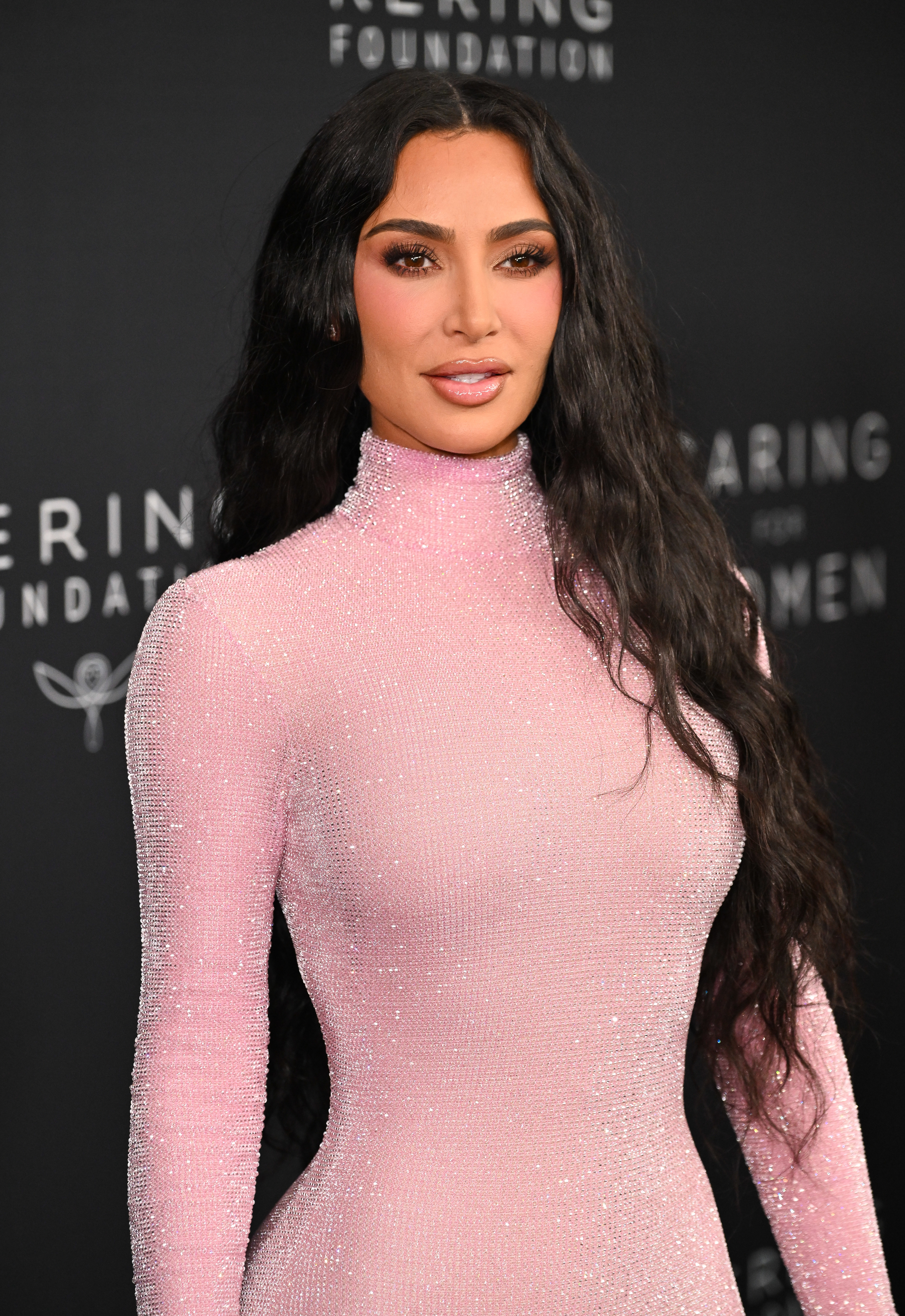 Close-up of Kim at a media event in a shiny, long-sleeved turtleneck outfit
