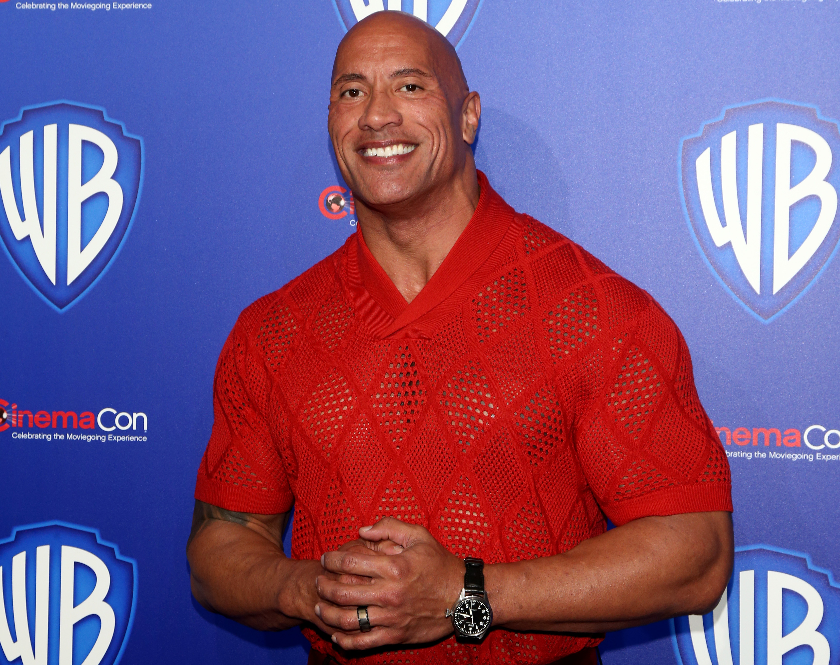 Close-up of The Rock at a media event wearing a short-sleeved shirt