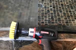 one of the brushes attached to a drill next to a shower pane with half still fogged up and the other super clear 