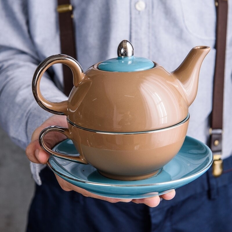 a hand holding the blue and brown tea set