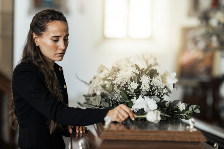A woman with her hand on a coffin at a funeral