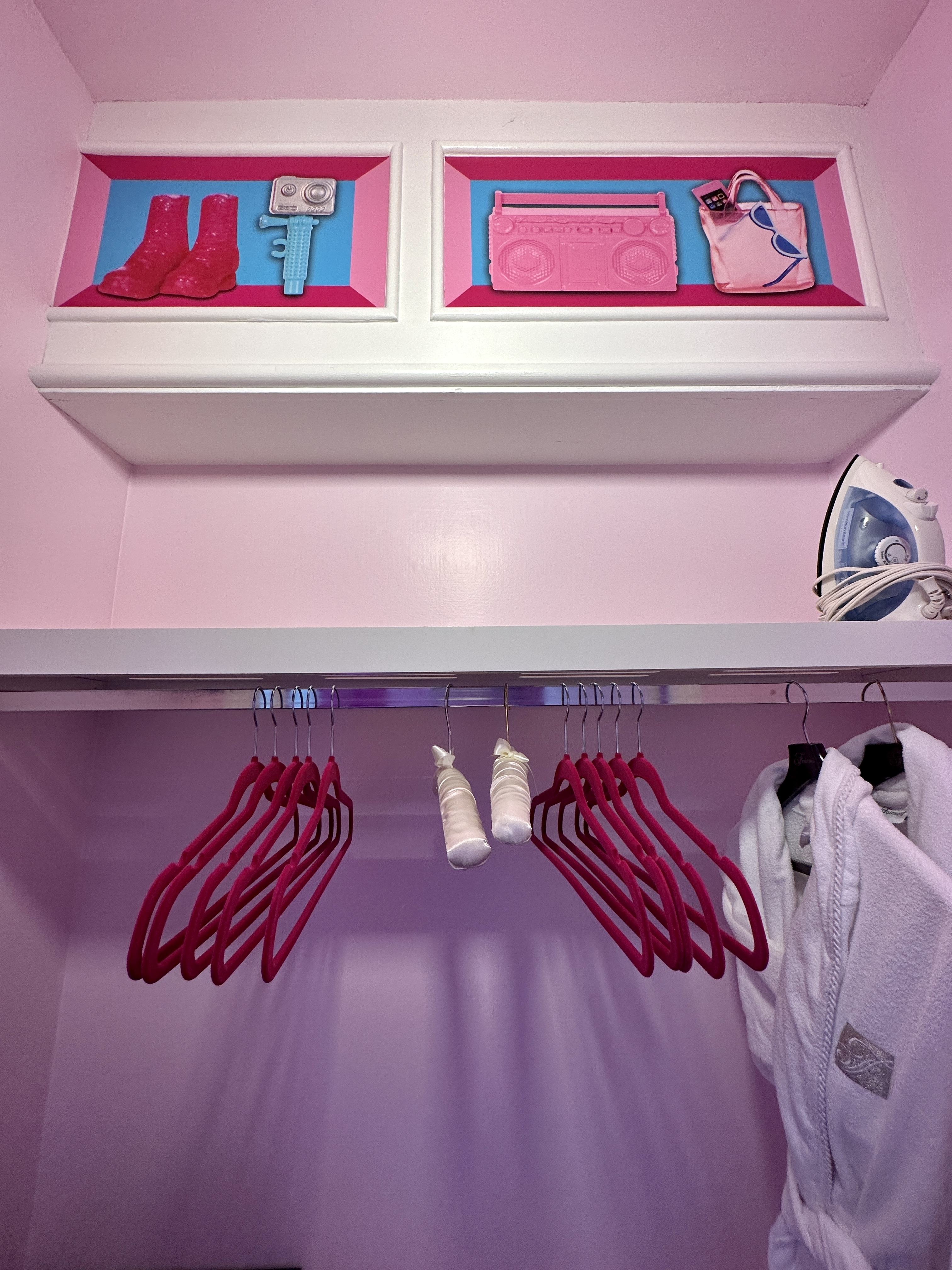 A pink closet with a robe and hidden art at the top
