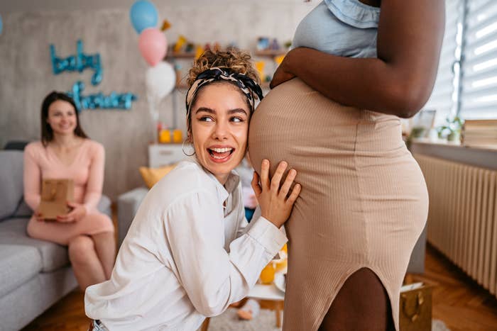 woman with her ear to her pregnant friend&#x27;s belly