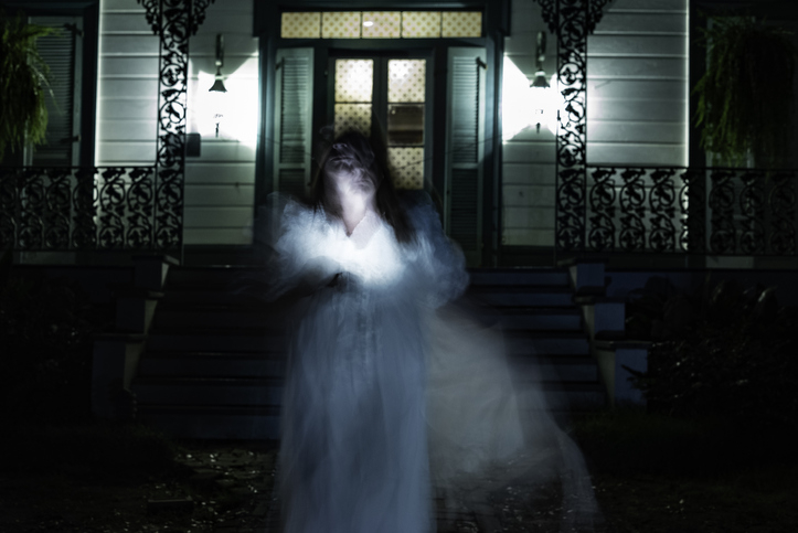 Blurred motion of a woman in long white gown in front of an old home