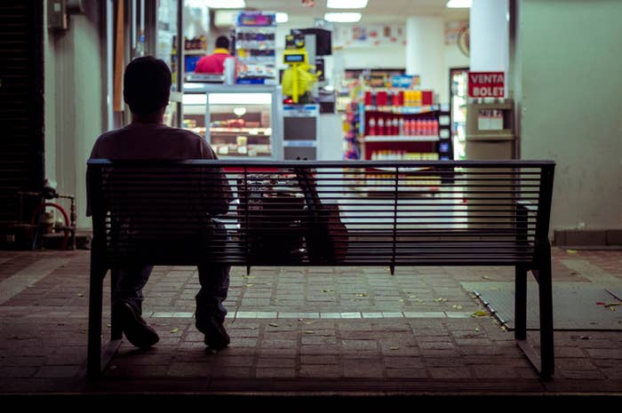 A person sitting on a bench outside of a convenience store
