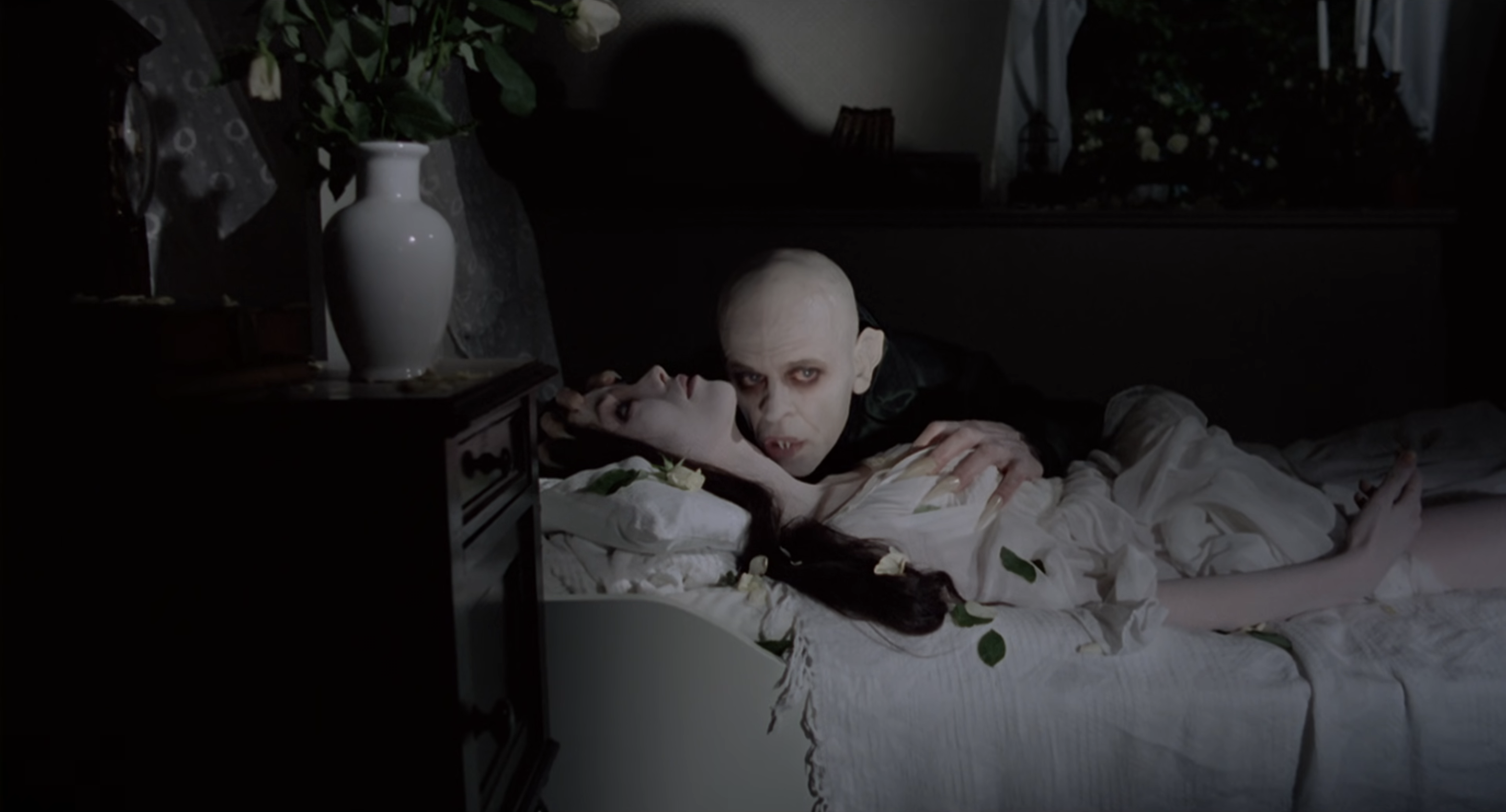 Nosferatu about to drink from the neck of Lucy, a woman lying in bed