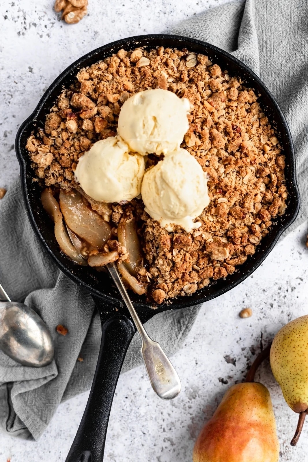 a pear crisp in a cast iron skillet topped with scoops of vanilla ice cream